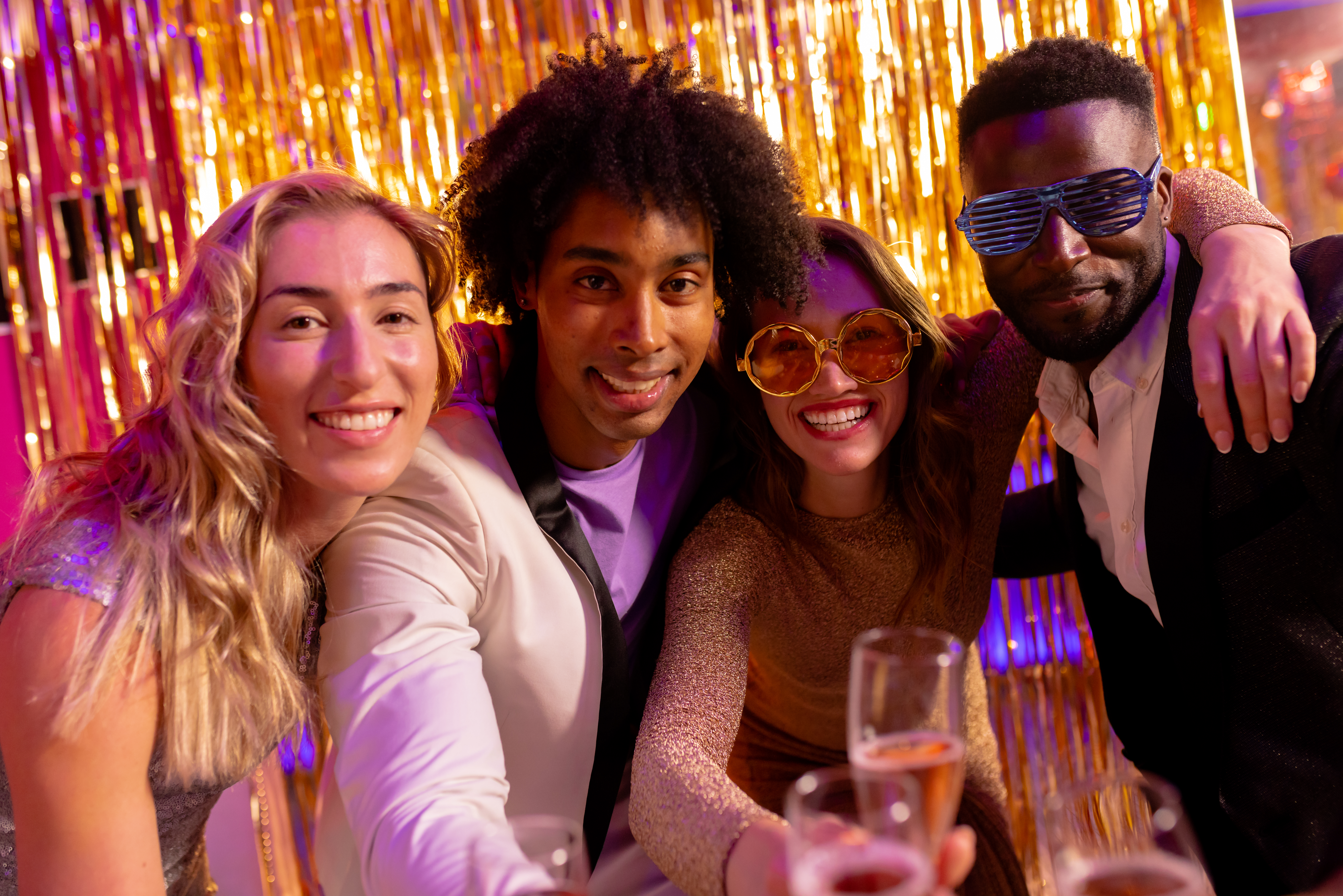 Portrait of four happy, diverse friends embracing and drinking champagne at a nightclub. Fun, drinking, going out, inclusivity and party concept.